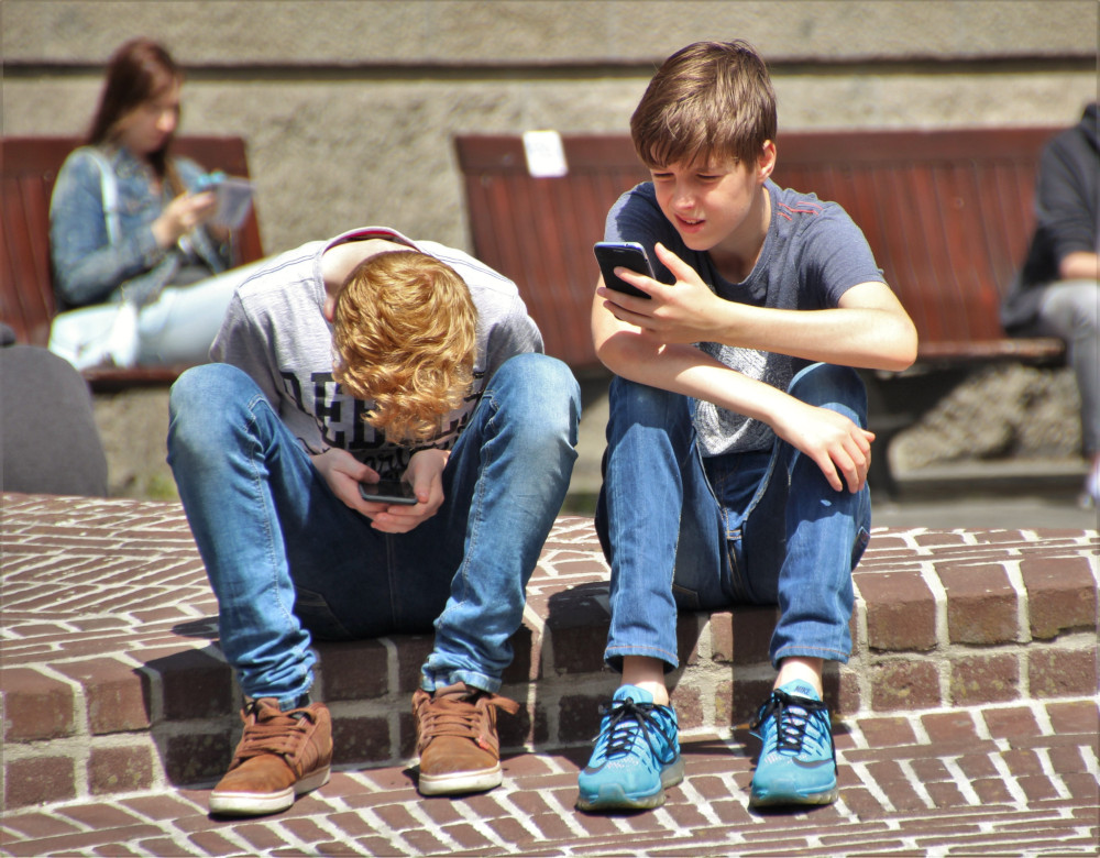 Deux adolescents utilisant leurs smartphones avec un forfait mobile neutre en CO2